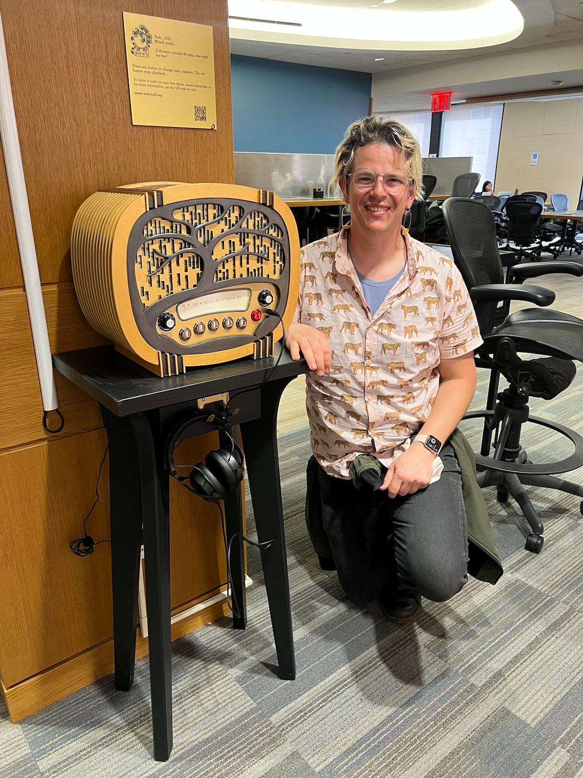 Sam kneeling next to what looks to be an old timey radio in Bobst library that plays RadLib Call Numbers Station